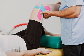 Physical Therapist moving patients knee with Kinesio tape treatment